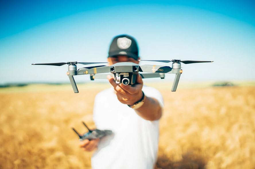 un homme avec t-shirt blanc et un casquette tenant un drone caméra dans ses mains