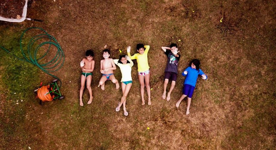 vue aérienne d'un groupe d'enfants alongés dans l'herbe qui font coucou au drone