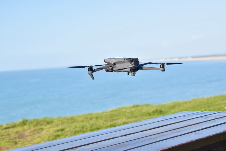 un drone mavic noir en plein vol au dessus dune table de picnic en face de locean
